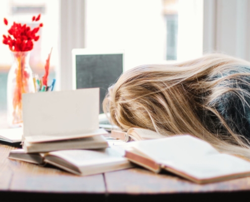 Frau legt den Kopf vor lauter mentalem Stress erschöpft auf den Schreibtisch, der übersät ist mit Arbeitsakten