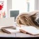 Frau legt den Kopf vor lauter mentalem Stress erschöpft auf den Schreibtisch, der übersät ist mit Arbeitsakten