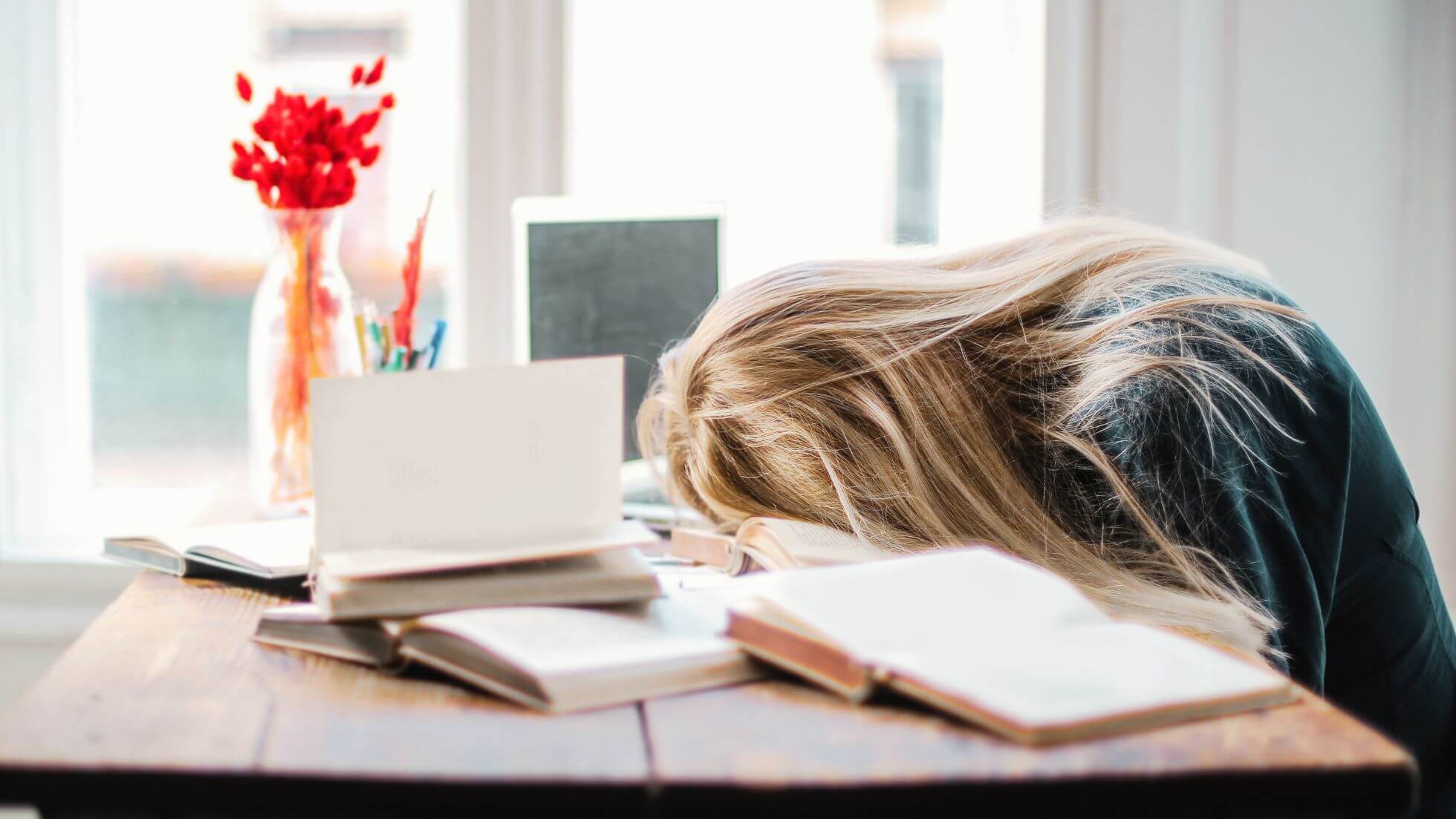 Frau legt den Kopf vor lauter mentalem Stress erschöpft auf den Schreibtisch, der übersät ist mit Arbeitsakten